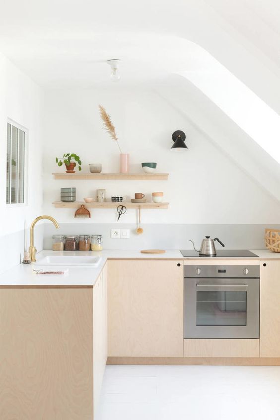 a Scandinavian loft kitchen with light-stained plywood cabinets, white countertops, open shelving, a skylight, and gold accents