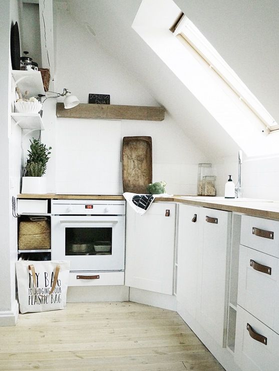 a small and neutral loft kitchen with white cabinets and leather handles, butcher block countertops and a wood slab shelf