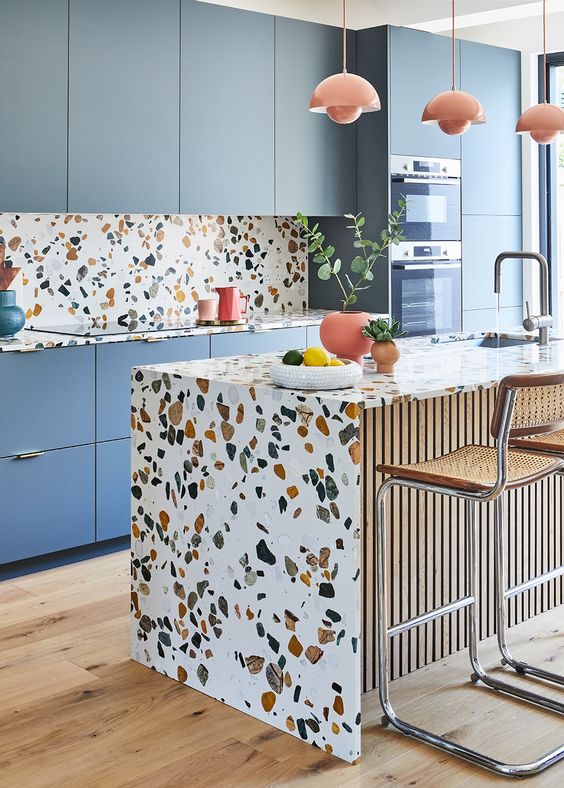 a cheerful blue kitchen with a bright terrazzo backsplash and countertops and coral pendant lamps and pots