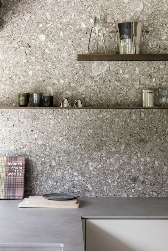 A minimalist gray kitchen with concrete countertops and a gray terrazzo backsplash with floating shelves is a chic space
