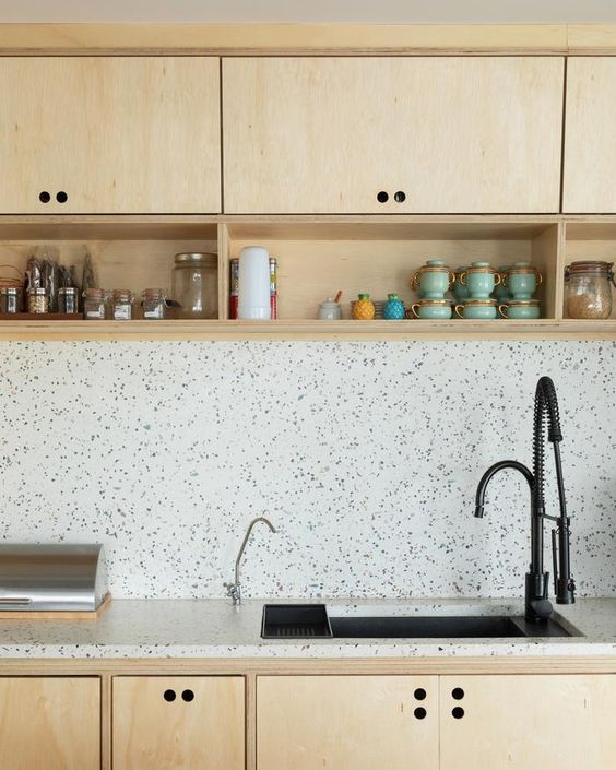A neutral plywood kitchen with white terrazzo backsplash and countertops and black fixtures for a more modern feel