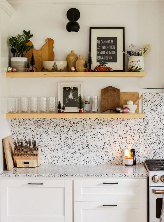 A white shaker style kitchen with black handles and a white terrazzo backsplash and countertop and floating shelves