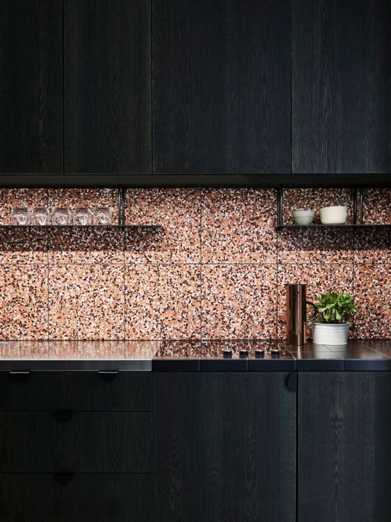 A sleek black kitchen with black countertops and a terracotta terrazzo backsplash is bold and cool