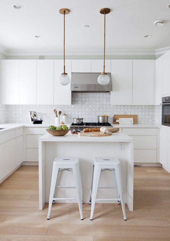 a modern white kitchen with printed tiles and a small kitchen island, chic pendant lamps and white bar stools