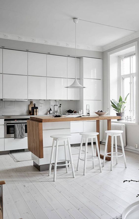 a glossy white minimalist kitchen with a gray countertop, a small kitchen island made of white and stained wood, white stools