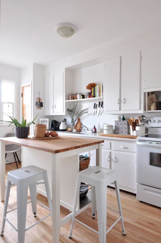 a beautiful crisp white kitchen with butcher block countertops, a small kitchen island that doubles as a dining area