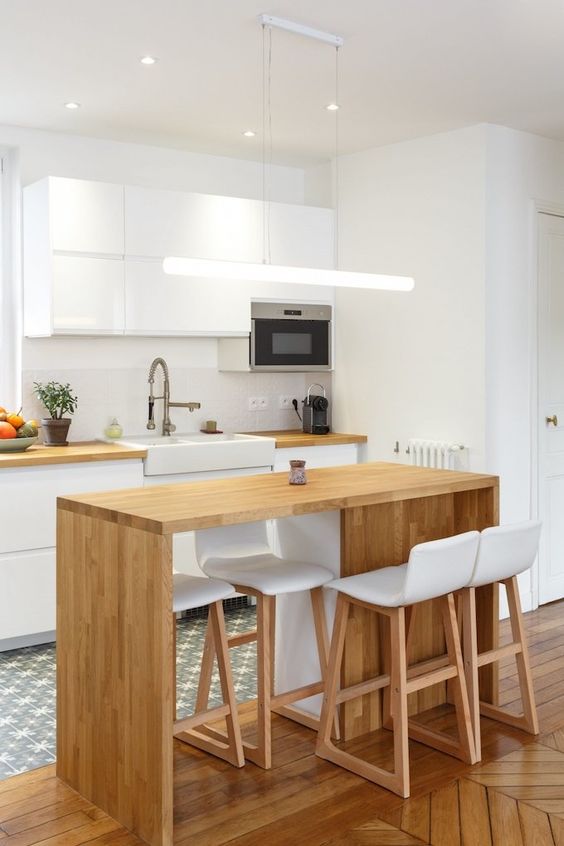 a minimalist white kitchen with butcher block wood countertops, a small, light stained kitchen island that matches the countertop