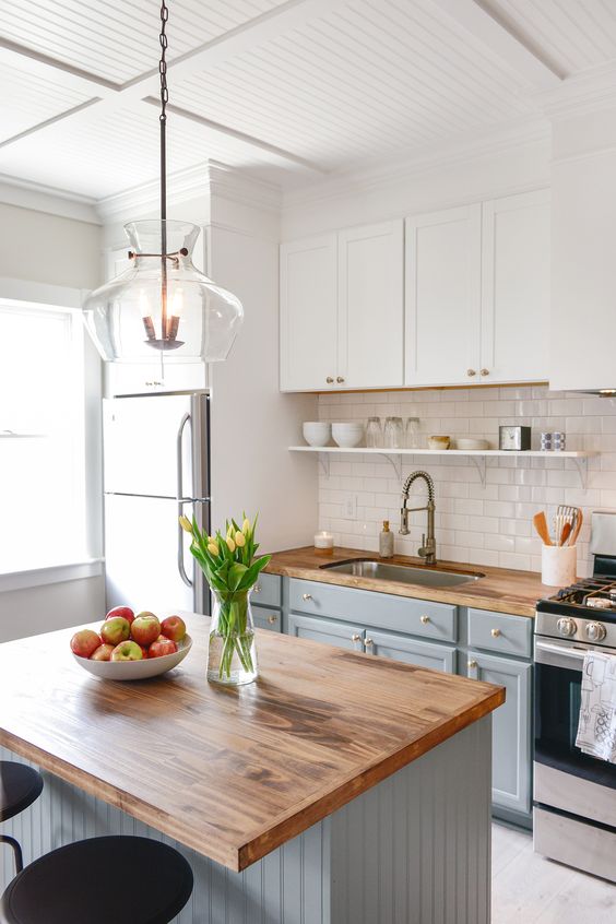 a modern two-tone kitchen with white subway tiles, butcher block countertops and a gray kitchen island with dining area