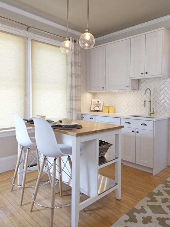 a small white kitchen with a herringbone backsplash, a small white kitchen island with a butcher block countertop and hanging lamps