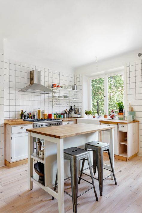 an inviting white modern kitchen with square tiles, butcher block countertops, a small kitchen island with storage and a dining area