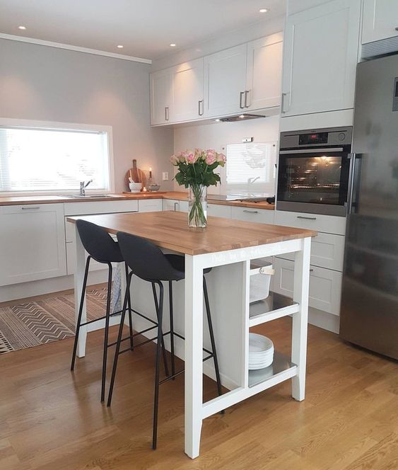a white kitchen with shaker style cabinets, a small kitchen island with storage and a dining area