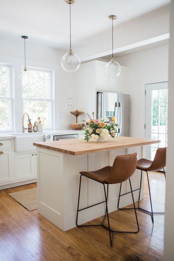 a sleek white kitchen with white countertops, matching kitchen island with butcher block countertop and leather stools