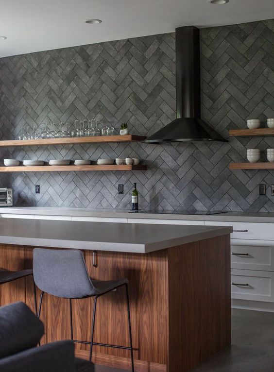 a modern kitchen with white cabinets, a stained island and gray stone countertops, and a herringbone concrete backsplash