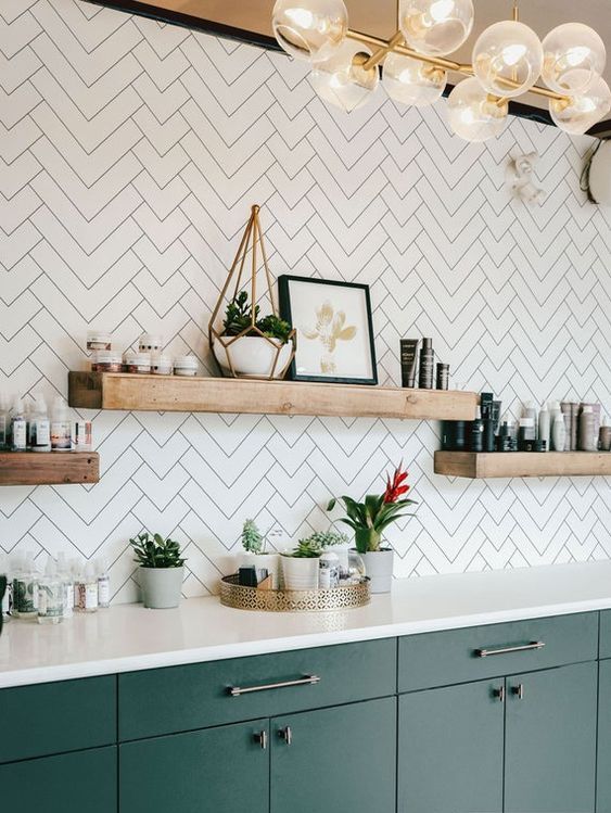 A green kitchen with white countertops and a white herringbone backsplash and floating shelves looks catchy