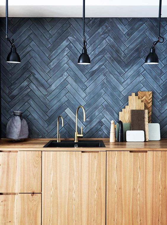 A light stained wooden kitchen with a slate gray herringbone backsplash and black vintage lamps across the room