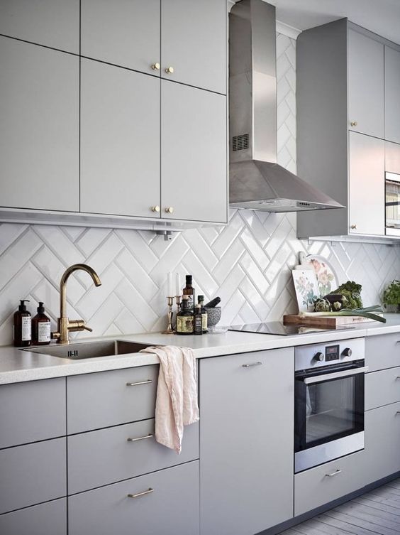 A minimalist dove gray kitchen with a glossy white herringbone backsplash and brass accents is a stylish and chic idea