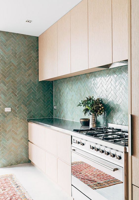 A minimalist, light-stained kitchen with a stainless steel countertop and a herringbone backsplash and feature wall for added interest