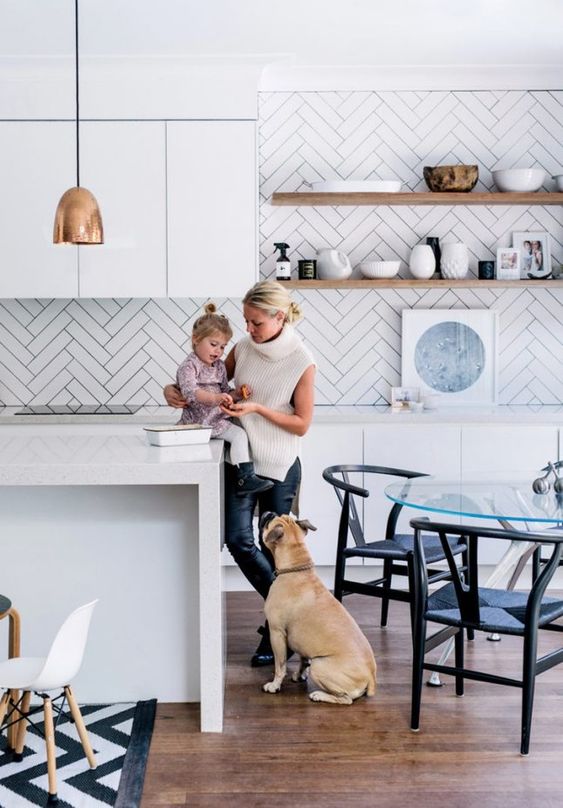 a minimalist white kitchen with sleek cabinets, white stone countertops, a white herringbone backsplash, and copper accents