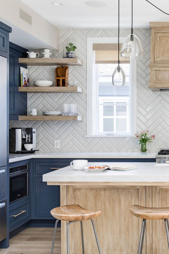 a sophisticated blue kitchen with a stained island and white countertops, a white herringbone backsplash and floating shelves