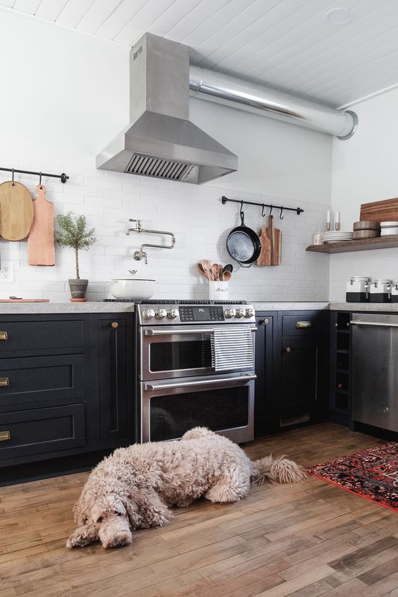 a black farmhouse kitchen with a concrete countertop, a white tile backsplash and stainless steel appliances