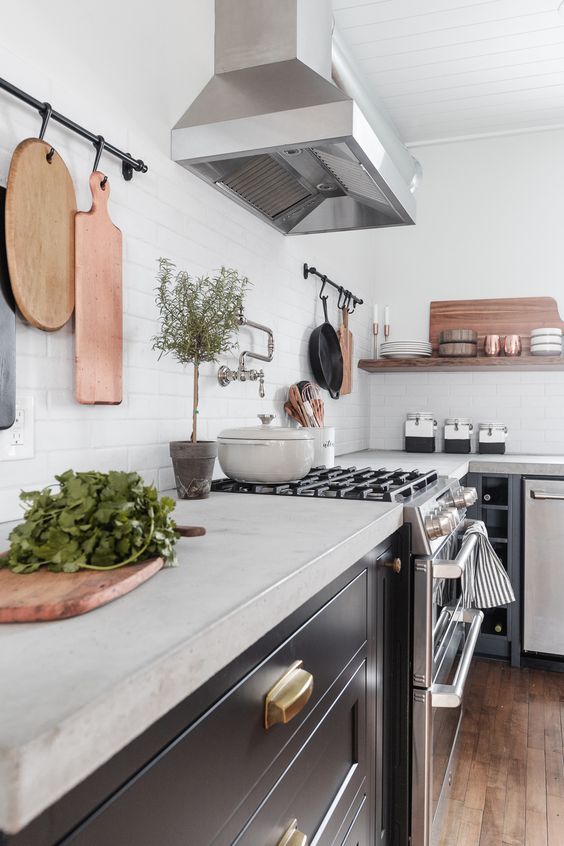 a black farmhouse kitchen with concrete countertops and a white backsplash and stained wood shelves