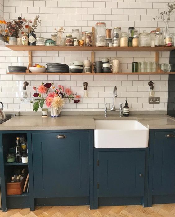 A navy farmhouse kitchen with concrete countertops, a white subway tile backsplash, and open wood shelving