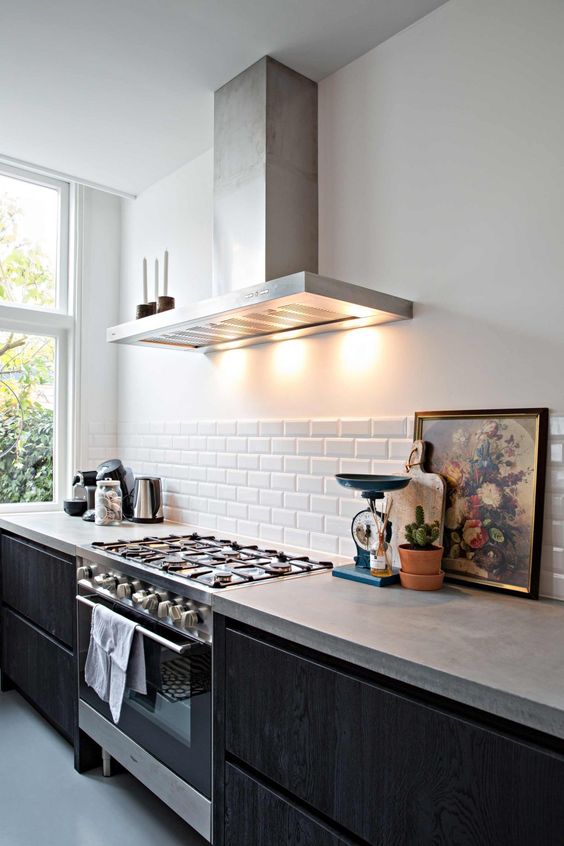 a Nordic black kitchen with sleek cabinets, concrete countertops, a white tile backsplash, and stainless steel appliances