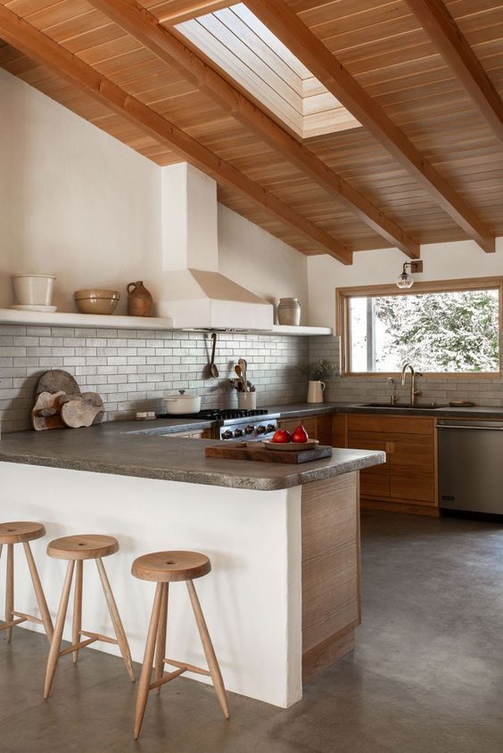 a rustic kitchen with stained cabinets, concrete countertops and a gray tile backsplash, and wooden beams on the ceiling
