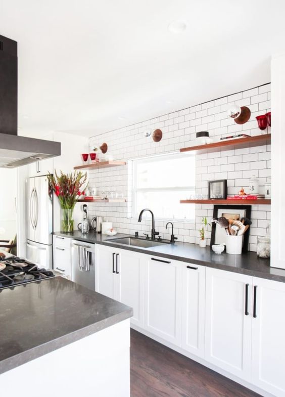 A white farmhouse kitchen with concrete countertops, black fixtures, and open shelving is an inviting space