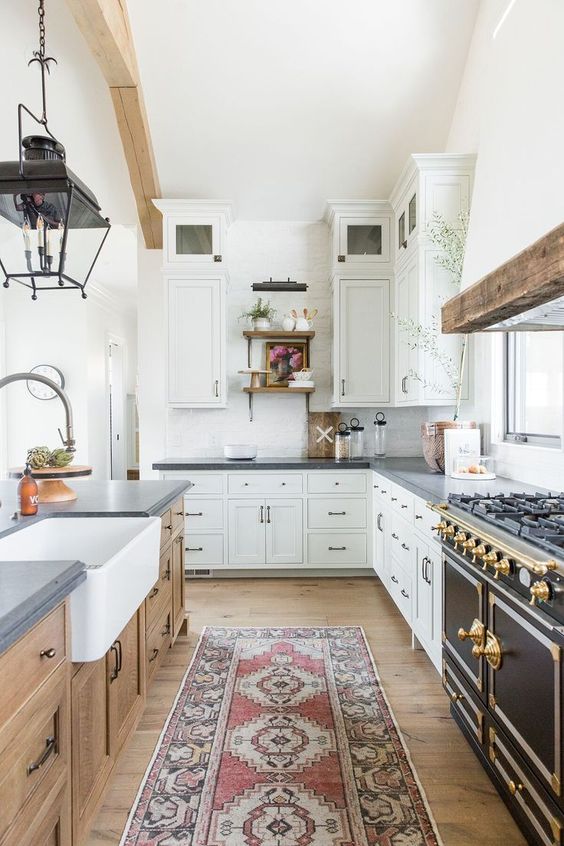 a white farmhouse kitchen with concrete countertops, a wooden island, a vintage stove and gold accents