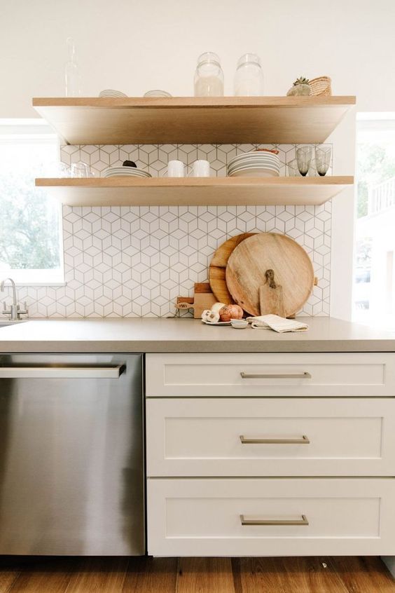 A white farmhouse kitchen with floating shelves, a white tile backsplash, and a concrete countertop is chic and inviting