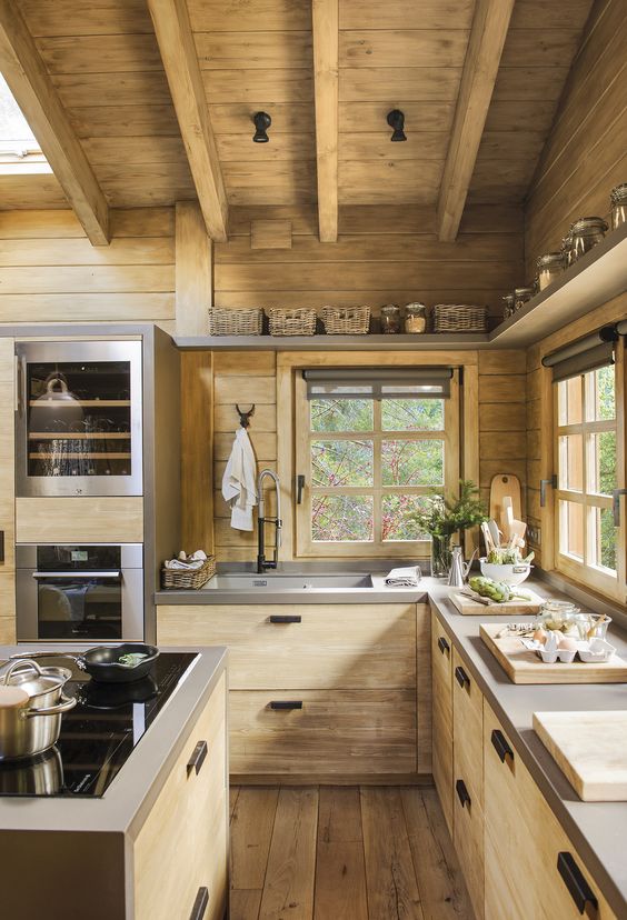 a wooden cabin kitchen with concrete countertops and wooden beams on the ceiling and black handles and knobs