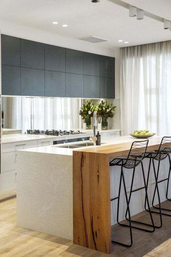 A chic two-tone black and white kitchen with a large kitchen island and additional wooden waterfall countertop for dining