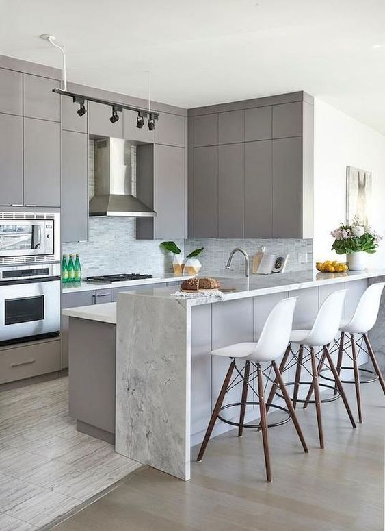 A minimalist gray kitchen with matching island and an additional raised white stone waterfall countertop for elegance