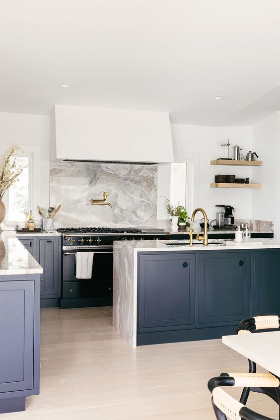 A sophisticated navy blue kitchen with gray stone countertops, including a waterfall countertop and backsplash, is very stylish