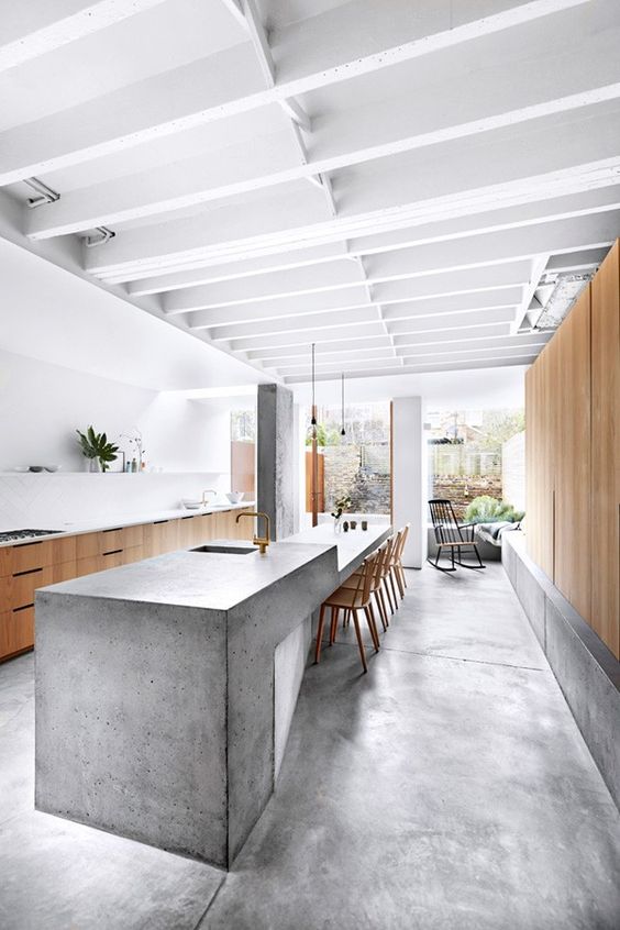a stylish, minimalist kitchen with handsome cabinets and a large kitchen island with a concrete waterfall countertop and brass hardware