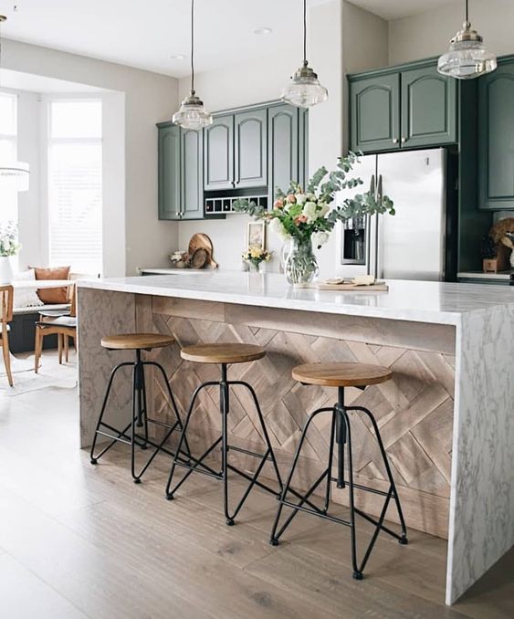A green vintage kitchen with a kitchen island with a white stone countertop and wood paneling and elegant pendant lamps