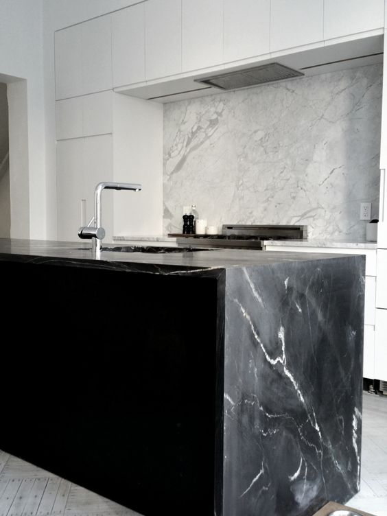 A white, minimalist kitchen with a contrasting black island and soapstone waterfall countertop is a chic idea