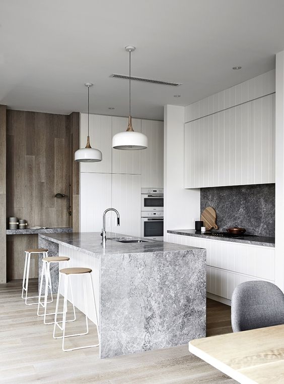 a sleek, minimalist kitchen with white cabinets, a gray stone backsplash, and a waterfall countertop
