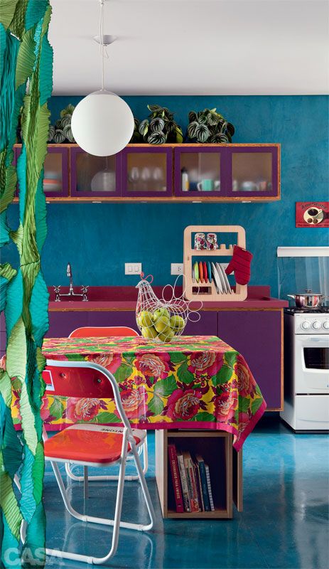 a colorful kitchen with blue walls, purple cabinets, a pink countertop and colorful chairs and linens