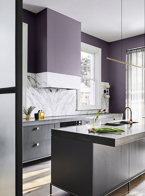 a dark purple kitchen with gray cabinets and white stone countertops and a splashback and touches of gold