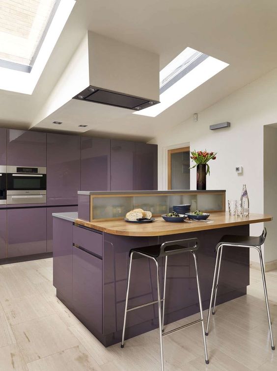A glossy purple kitchen with stone and butcher block countertops, a range hood and skylights is very stylish