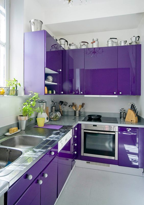 A stunning glossy purple kitchen with gray stone countertops and white knobs is a very bold and eye-catching space