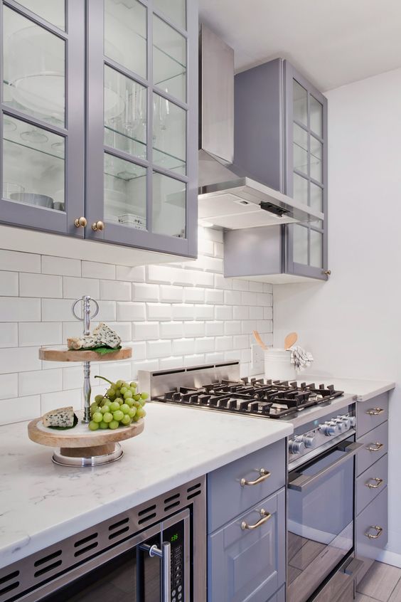 A pretty purple kitchen with a white subway tile backsplash and white countertops and brass and gold accents