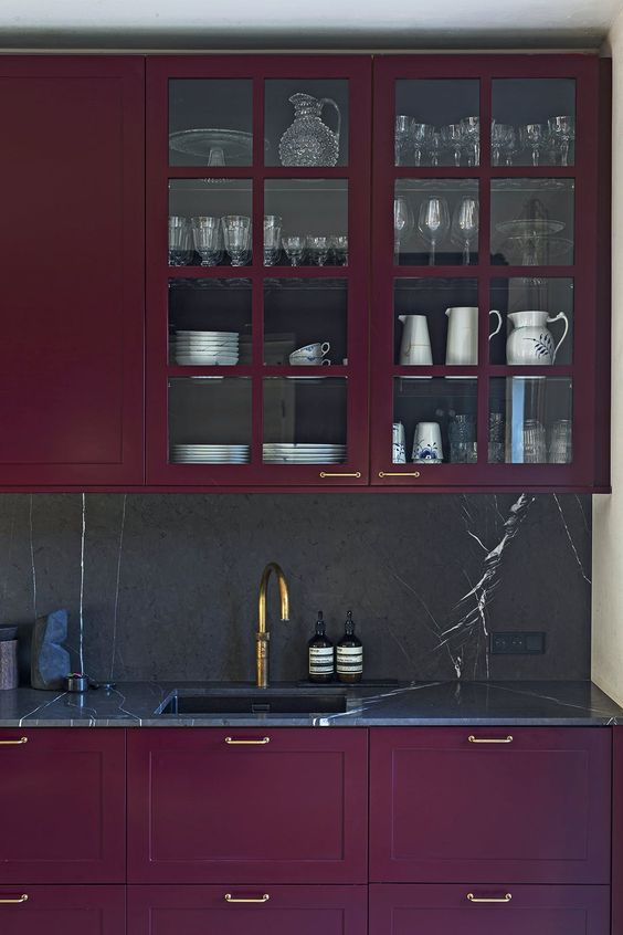 A sophisticated deep purple kitchen with a black marble backsplash and countertops and gold accents for an exquisite ambience
