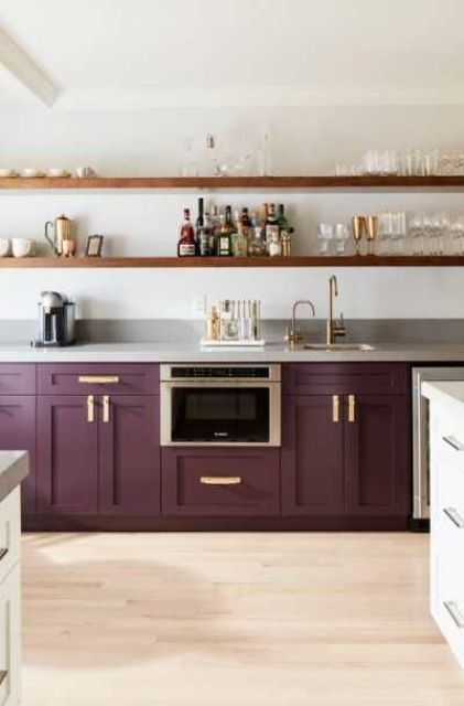 A stylish deep purple kitchen with vintage cabinets, gray stone countertops and long open shelves, and gold accents