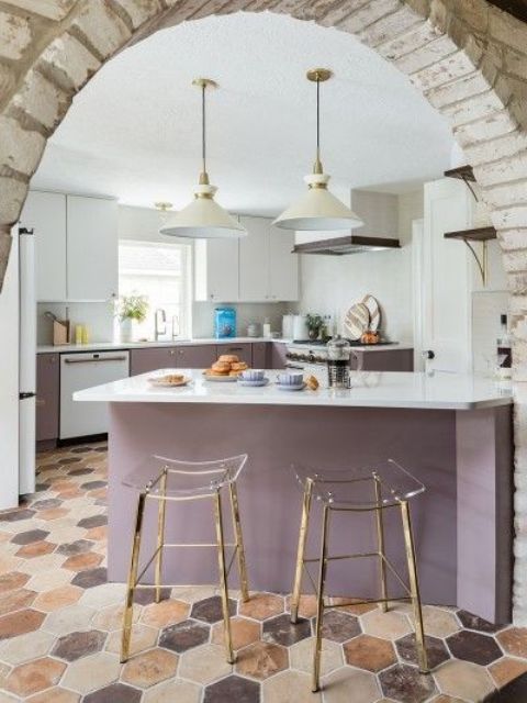 A stylish white and purple kitchen with white countertops and backsplash and clear acrylic stools on gold legs