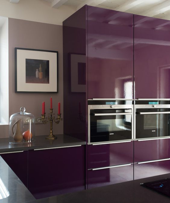 A gorgeous purple kitchen with glossy finishes, gray stone countertops, and pretty art is chic and bold
