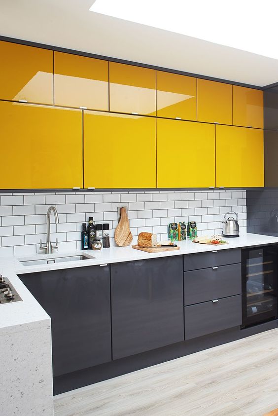 A bold, minimalist kitchen with graphite gray base cabinets and bold yellow upper cabinets, plus a white subway tile backsplash