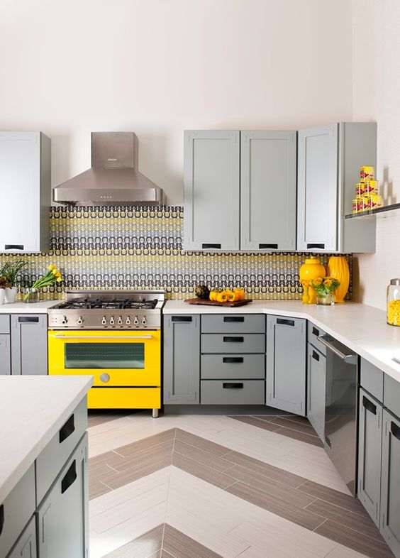 A cheerful, modern kitchen with light gray cabinets, a striking yellow stove, chevron tile flooring, and a colorful tile backsplash